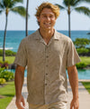 Man wearing a brown patterned shirt with palm trees and ocean in the background
