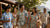 Group of people in Honolulu wearing authentic, well-fitted Hawaiian shirts and a floral dress in natural tones while walking through a local neighborhood market
