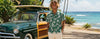 man wearing an Aloha Shirt with white pants in a sunny day with a 11950 Ford Woody Hot Rod Surf Wagon with a long board and the ocena in the background