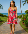 Young woman in a coral floral dress walking on a path with palm trees and ocean in the background